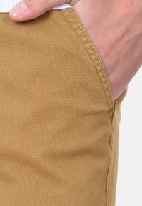 Pantaloni khaki realizzati in cotone testurizzato, con un design a gamba dritta e tasca laterale, con cuciture visibili e leggere variazioni di colore.