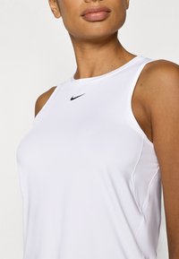 Λευκό αμάνικο αθλητικό τοπ από λείο, ελαφρύ ύφασμα, με μαύρο λογότυπο Nike στην επάνω περιοχή του στήθους και διακριτικές λεπτομέρειες στις πλαϊνές ραφές.