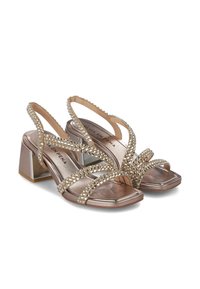 Tacones slingback de bronce metálico con tacón cuadrado, adornados con piedras de strass transparentes y con un diseño de tiras entrelazadas.
