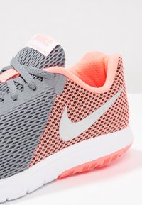 Parte superior de malla gris con acentos en rosa brillante, con entresuela blanca y suela exterior rosa. Logo plateado en el lateral, cordones texturizados y cuello acolchado.