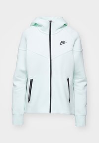 Mint green Nike zip-up hoodie with a high collar, black zipper, and two zippered side pockets. Features contrasting stitching and logo.
