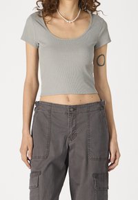 Šedý žebrovaný crop top s krátkými rukávy spárovaný s volnými šedými cargo kalhotami s velkými kapsami a viditelnými švy.