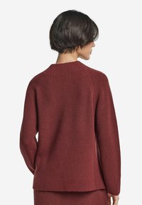 Körsbärsröd stickad tröja med ribbad struktur, raglanärmar och rundad halsringning, med en avslappnad passform och rak nederkant.