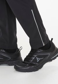 Zwarte sportieve schoenen met een bovenwerk van mesh, een gestructureerde zool en reflecterende accenten. De broek heeft een ritsopening en een zijstreepdetail.