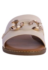 Sandalia tipo slide beige de punta abierta con un upper liso, detalle de cadena de metal en dorado y una suela marrón acolchada con acentos de costura.