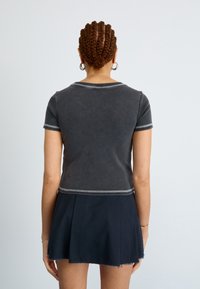 Top cinza de mangas curtas com decote redondo e costuras em contraste, combinado com uma saia azul marinho escura com bainha desfiada.