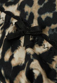 Tissu à imprimé léopard avec un mélange de couleurs beige et noir, orné d'un petit nœud noir et de couture décorative le long du bord.