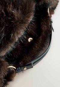 Geantă de mână din blană maro, cu o curea din piele neagră lucioasă și accesorii din aur. Prezintă o textură moale și un sistem de închidere cu capse circulare.
