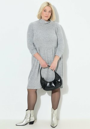 Graues knielanges Kleid mit hohem Kragen und langen Ärmeln; kombiniert mit einer schwarzen Handtasche und silbernen Ankle Boots. Glatte Textur.