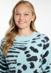 Jasnoniebieski puszysty sweter z czarnym wzorem w panterkę, okrągłym dekoltem i długimi rękawami. Miękka struktura i luźny krój.
