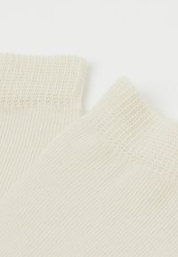 Beiga bomullssockor med ribbad mudd, mjuk textur och en slät finish. Designen inkluderar subtila stickmönster för extra detalj.