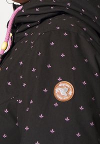 Czarna kurtka z małymi fioletowymi wzorami kwiatowymi. Posiada teksturowaną skórzaną naszywkę z motywem ptaka oraz kaptur z różowym sznurkiem.