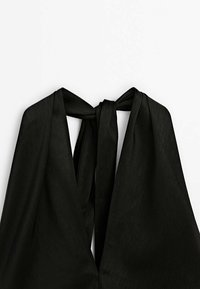 Vêtement noir sans manches avec un col en V profond et un détail de nœud en tissu à l'arrière du cou.
