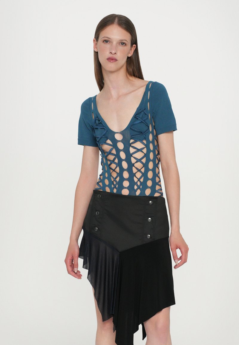 Blue knit top with cut-out patterns and bows, paired with a black asymmetrical skirt featuring buttons and layered textures.