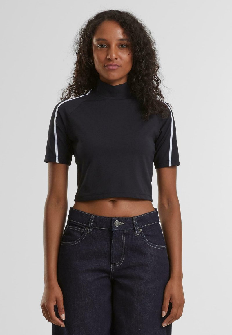Svart kort topp med høy hals, korte ermer og hvite side stripes. Glatt stoff med figurnær design. Kombinert med mørke jeans.