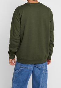 Sudadera verde oliva con cuello redondo, puños y dobladillo acanalados. Textura suave, ajuste relajado y detalle de costuras visibles en la espalda.
