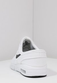 Chaussure de sport blanche avec une tige en mesh texturé, un col rembourré et un logo swoosh noir. Comprend une semelle coussinée avec une unité d'air visible.