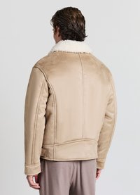 Giacca beige in ecopelliccia effetto shearling con una texture morbida, caratterizzata da un ampio colletto bianco, spalle strutturate e tasche laterali.