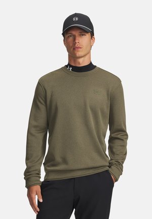 Olivegrünes Langarmshirt mit strukturiertem Muster, Rundhalsausschnitt und gesticktem Logo. Kombiniert mit einer schwarzen Mütze mit weißer Naht.