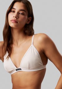 Hvid ribbet trekants-bh med tynde stropper og et Calvin Klein logo-patch i midten. Blød tekstur og minimalistisk design.