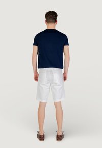 T-shirt à manches courtes bleu marine, shorts blancs ajustés et chaussures décontractées marron. Matériau en coton, design ajusté et lignes épurées.
