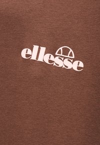 Καφέ πλεκτό ύφασμα με λευκό λογότυπο «ellesse» και κεντημένο σχέδιο ημικυκλίου στο κέντρο.