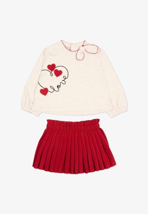 Top beige chiaro a manica lunga con cuore rosso e design "love", abbinato a una gonna rossa plissé, adatto a un bambino.