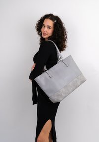 Gray tote bag with a smooth top and textured gray bottom, featuring two short handles and a sleek design. Simple and modern with subtle branding.