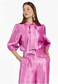 Bright pink satin blouse with a large collar, puffed sleeves, and a bow tie at the neck, paired with matching high-waisted trousers.