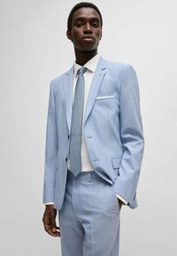 Completo azzurro chiaro dal taglio slim, con righe sottili, una camicia bianca e una cravatta a fantasia. Dettagli di cucitura e tasche di rilievo.