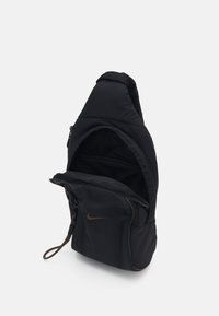 Geantă de umăr neagră, fabricată dintr-un material moale, cu un compartiment principal cu fermoar, un design elegant și un accent al logo-ului Nike de culoare maro.