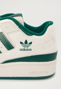 Bijela tenisica s zelenim akcentima, glatka kožna gornja površina, teksturirane bočne trake, podstavljeni ovratnik te logotip na peti i bočnim stranama.