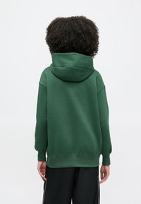 Zielona bluza z kapturem wykonana z miękkiego materiału, z kapturem na sznurek, długimi rękawami, ściągaczami na końcach rękawów oraz luźnym fasonem.