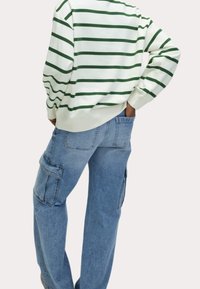 Weißes Sweatshirt mit grünen Streifen, kombiniert mit hellblauen Cargo-Jeans mit Seitentaschen und lockerem Schnitt. Lässiges und bequemes Outfit.