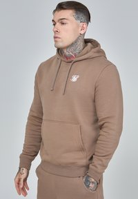 Brown cotton hoodie with a front pocket, drawstring hood, and a white logo on the chest. Smooth fabric with ribbed cuffs and hem.