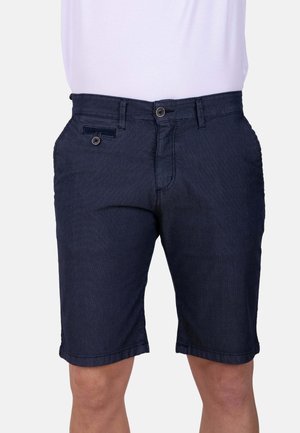 Hombre que lleva pantalones cortos casuales de color azul oscuro hasta la rodilla con cierre de botón y cremallera, combinados con una camisa de color claro metida.
