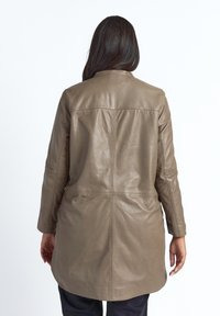 Bruine leren jas met een licht gebogen zoom, lange mouwen en een eenvoudige kraag. Heeft een gladde textuur en geen zichtbare metalen onderdelen.