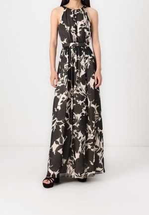 Kvinde iført en ærmeløs, sort-hvid blomster maxi-kjole med markeret talje og sorte plateau sandaler.