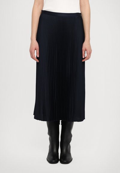 Jupe midi plissée en bleu marine foncé, dotée d'une taille lisse et d'une texture fluide, associée à des bottines noires élégantes.