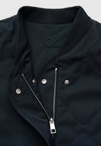 Schwarze gesteppte Jacke mit geripptem Kragen, teilweise geöffnetem silbernem Reißverschluss und silbernen Druckknöpfen an der vorderen Verschlussleiste.