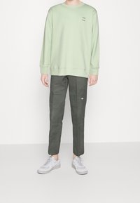 Sweat-shirt vert clair à col rond avec un logo minimaliste, associé à un pantalon cargo vert foncé à jambes fuselées avec des accents cousus. Baskets blanches.