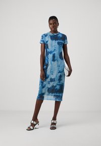 Modrá tie-dye midi šaty s priliehavým strihom a krátkymi rukávmi, s hladkou, lesklou textúrou a okrúhlym výstrihom. Strieborné sandále na vysokom podpätku.