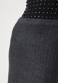 Material tricotat cu dungi de culoare gri cărbune, evidențiind un talie elastică. Vedere detaliată care subliniază textura și materialul moale, fără distrageri.