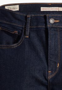 Jean skinny super haute en denim bleu foncé avec des coutures orange, une poche avant et un bouton métallique sur la ceinture.