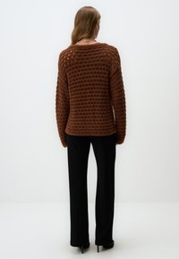 Bruine gebreide trui met een textuur, open-stikpatroon, met lange mouwen en een ronde hals, gecombineerd met zwarte slim-fit broek.