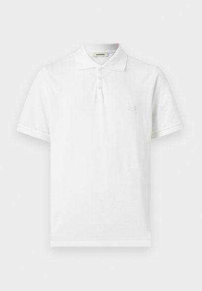 Polo blanc à manches courtes avec trois boutons, col classique et petite écusson logo sur la poitrine gauche.