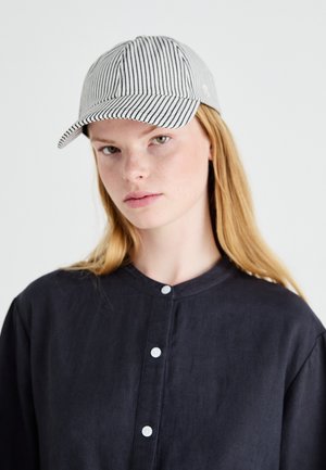 Striped cap in black and white cotton, featuring a curved brim and a button closure, worn with a buttoned dark shirt.
