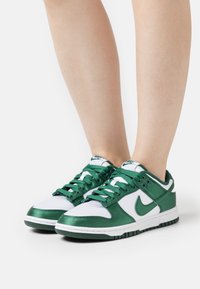 Zelené a bílé tenisky s hladkým povrchem, se saténovým leskem, kulatou špičkou a kontrastními tkaničkami. Logo Nike viditelné na boku.