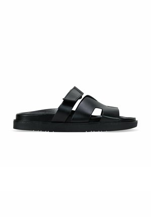 Sandalia negra con acabado mate, dos tiras cruzadas con detalles troquelados y una suela plana texturizada para mayor agarre. Diseño elegante y moderno.