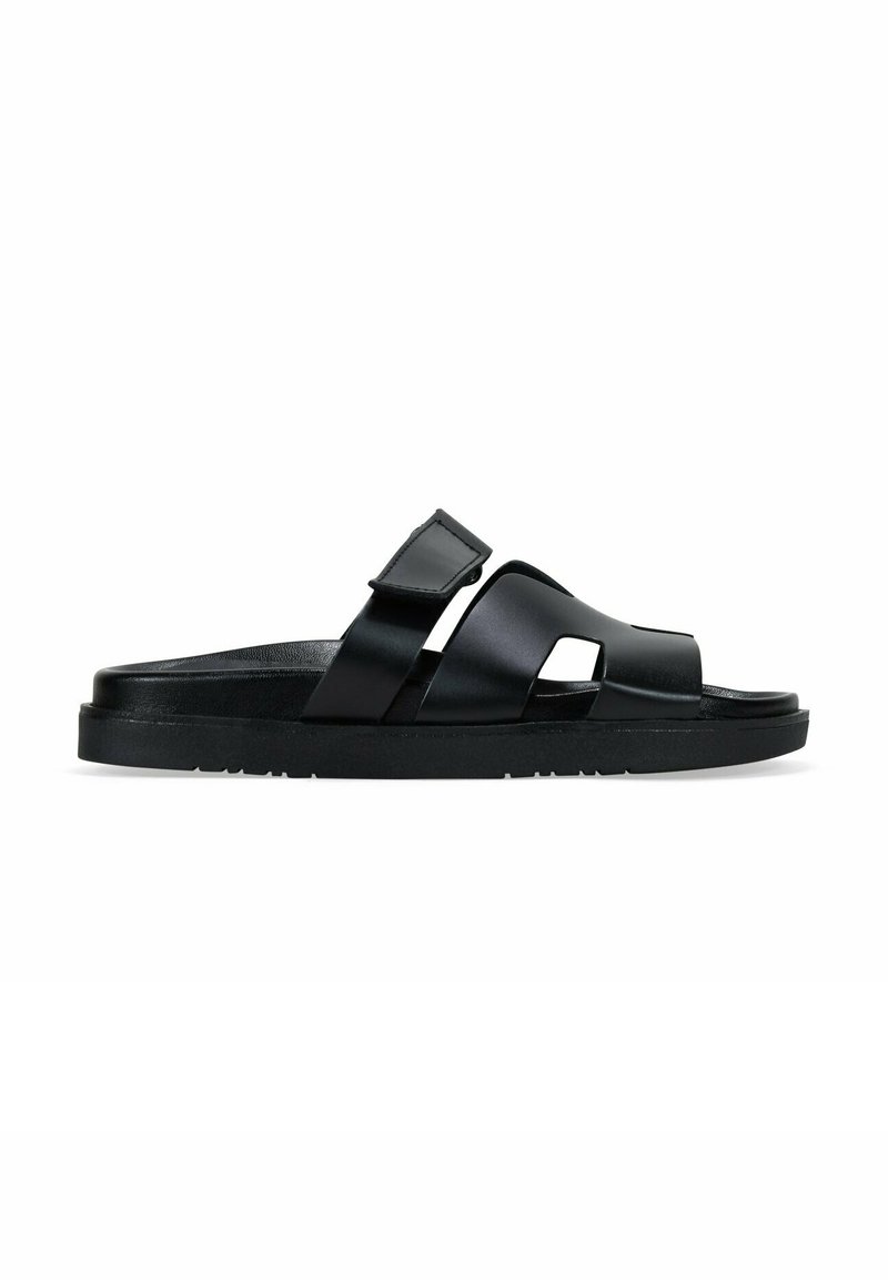 Sandalia negra con acabado mate, dos tiras cruzadas con detalles troquelados y una suela plana texturizada para mayor agarre. Diseño elegante y moderno.